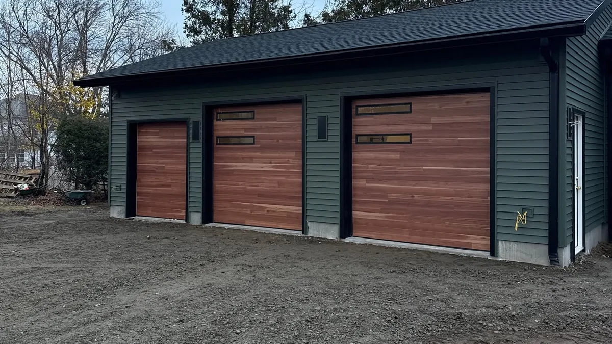 Three wood-look garage doors with upper windows on a green-sided garage.
