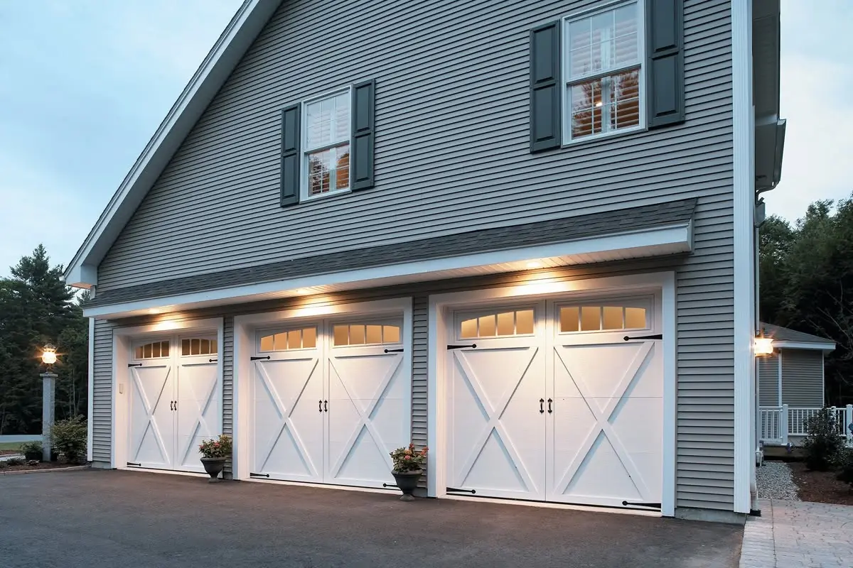 Three white carriage-style garage doors on a gray house at dusk.