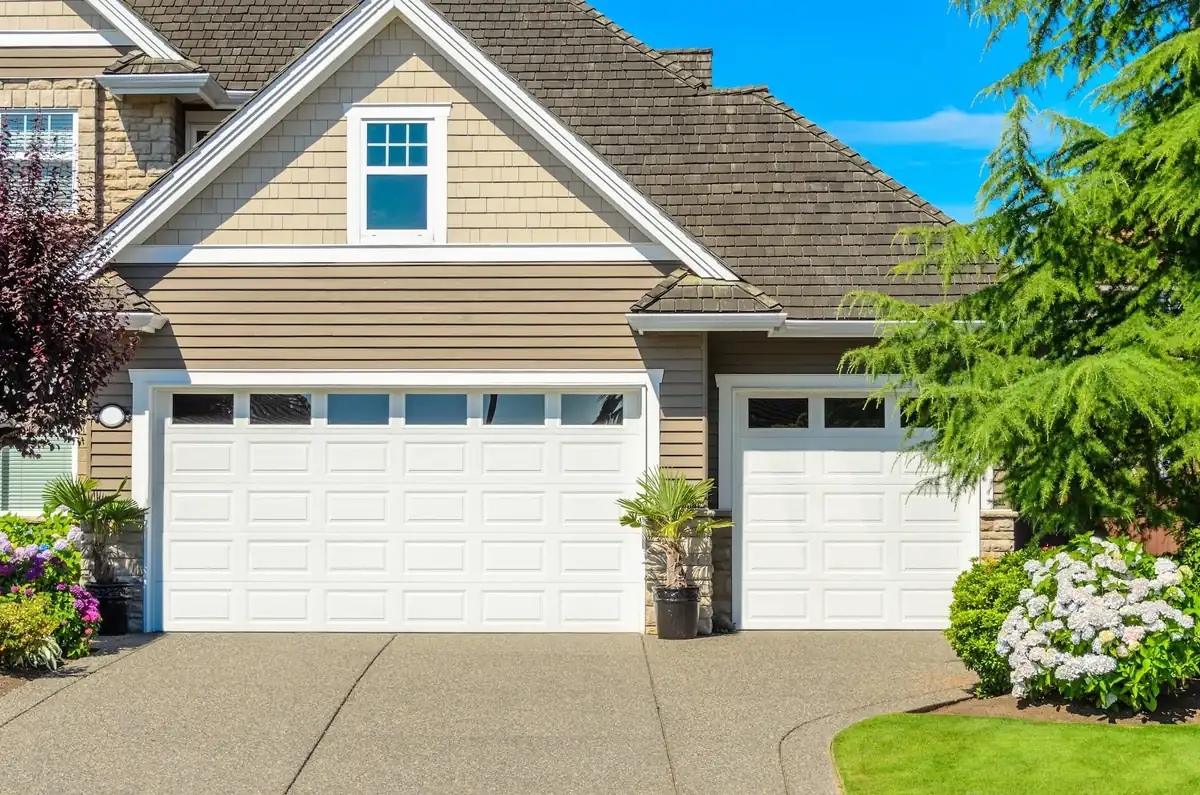 White raised-panel garage doors with upper windows beside a landscaped driveway.